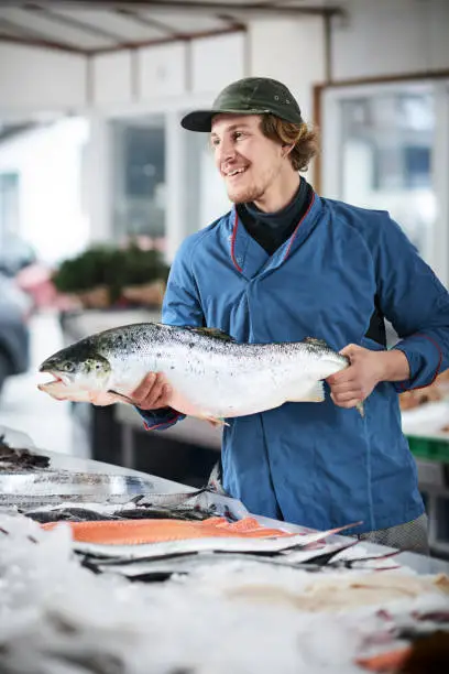A young male shop assistant in a fishshop saling fresh fish