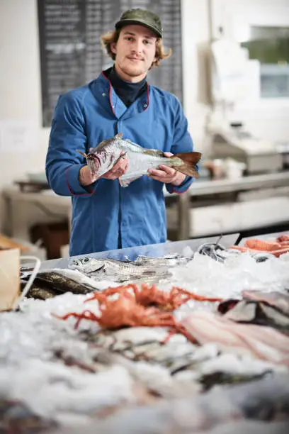 A young male shop assistant in a fishshop saling fresh fish