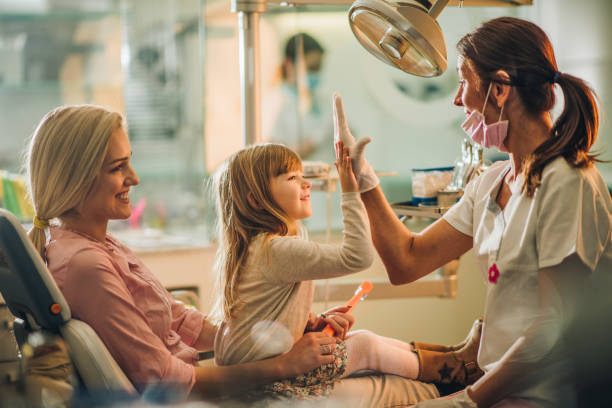 Give me high-five, you were great at dental exam! Happy girl with her mother giving high five to a dentist after medical exam at dentist's office. Family Dental Care stock pictures, royalty-free photos & images