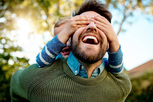 Humorous and candid scene with a young man in a beanie and yellow jacket playfully covering a woman's mouth, both showing playful expressions