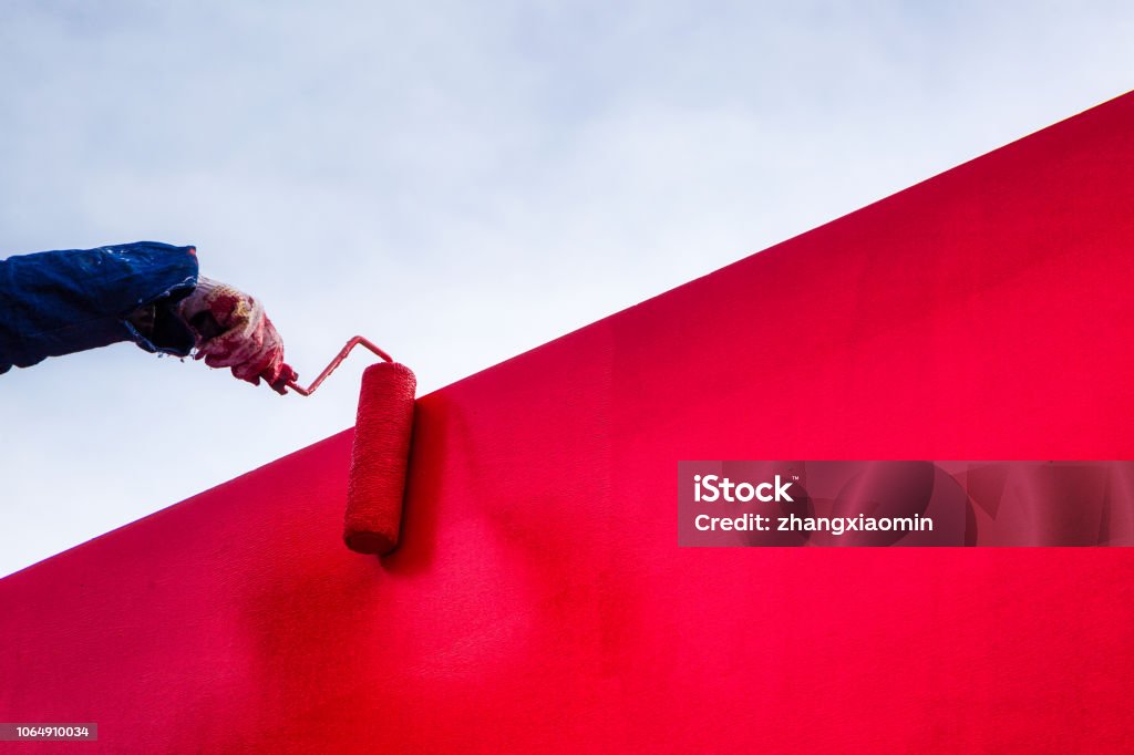 Red latex paint stucco wall Workers decorate the exterior wall to paint the city rose, the color is very comfortable, if you paint more than two times to ensure the color is dazzling Painting - Activity Stock Photo