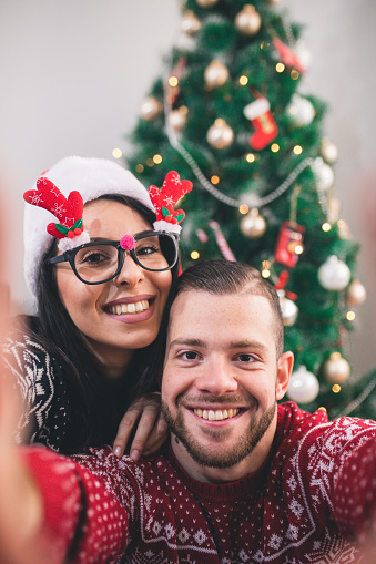 Capturing a happy moment. Beautiful young loving couple bonding to each other and smiling while making selfie with Christmas Tree in the background