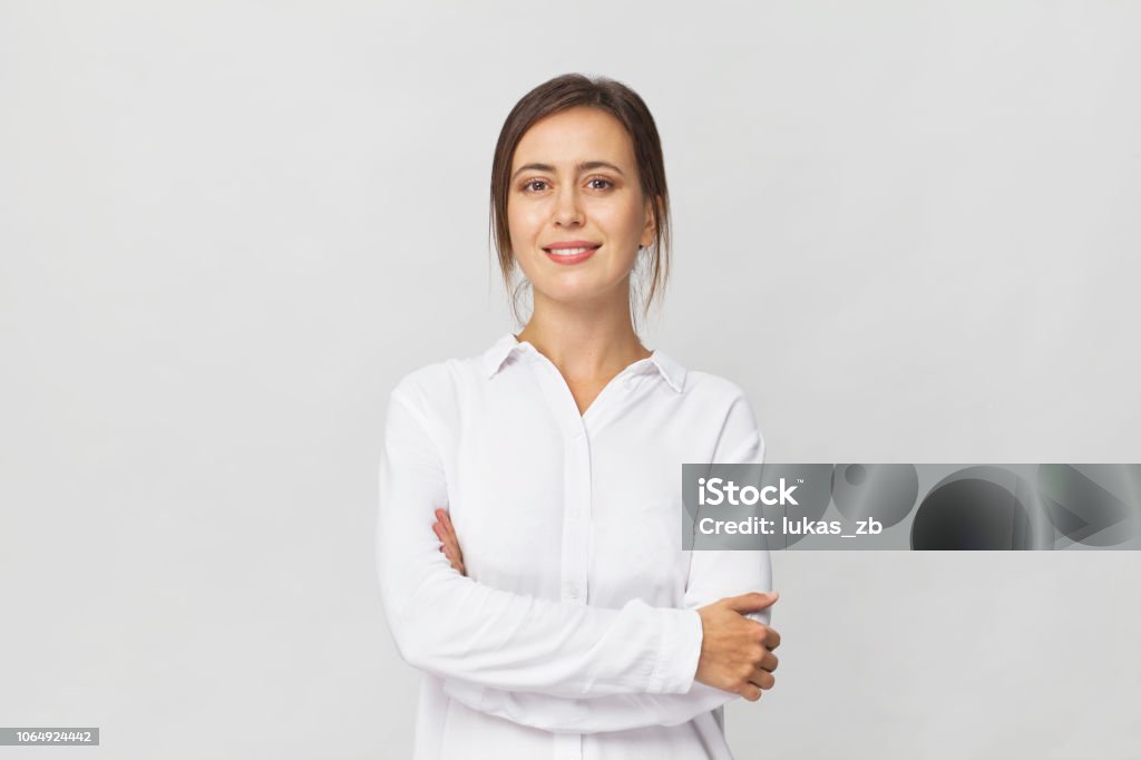 Young confident brunette woman in white elegant shirt smiling portrait against white background Amazing and cheerful smiling brunette in white shirt studio shot, isolated on white Women Stock Photo