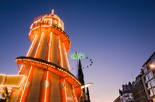 Winter festival fairground attractions in Edinburgh, Scotland, part of Edinburgh's Christmas and Edinburgh's Hogmanay 2016. A brightly coloured helter-skelter, with high-rising Star Flyer swing ride in the background next to the Scott monument.