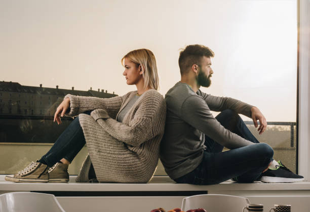 istock Young couple sitting back to back on a window sill while having relationship difficulties. 1064926270