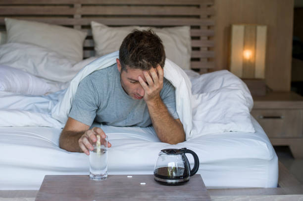 portrait de maison mode de vie des jeunes épuisé et gaspillé homme réveille souffrant de maux de tête et la gueule de bois après avoir bu de l’alcool à la soirée allongé sur le lit des malade et misérable encore ivre - alcohol drug abuse alcoholism pill photos et images de collection