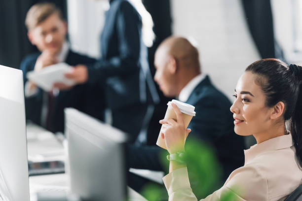 istock smiling young businesswoman holding disposable coffee cup while working in open space office 1064930772