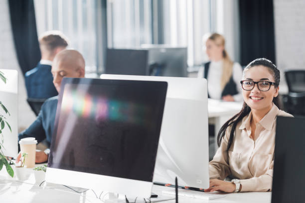 istock close-up view fo desktop computers and young businesswoman smiling at camera while working with colleagues in open space office 1064930790