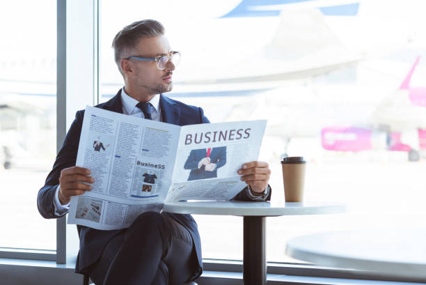 empresario adulto leyendo periódico y mirando a la ventana en el aeropuerto - airport newspaper travel business travel fotografías e imágenes de stock