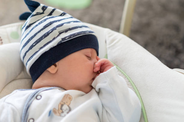 istock Sleeping baby in swing automatic electrical chair and sucking left thumb 1064936500