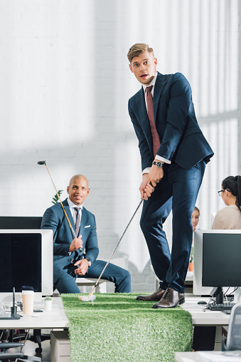 young multiethnic businessmen playing golf in open space office