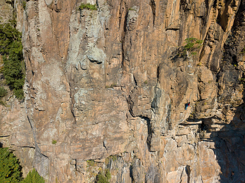 Young Japanese man rock climbing in an extreme location op a huge rock face