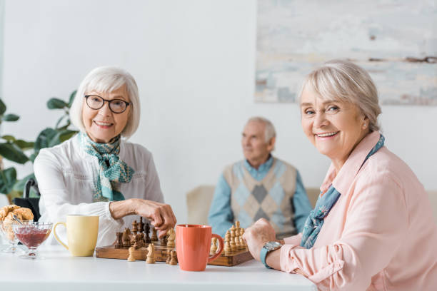 istock senior women playing chess and drinking coffee while senior man sitting on sofa 1064954872