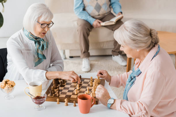 istock senior women playing chess and drinking coffee while man reading book on sofa 1064954874
