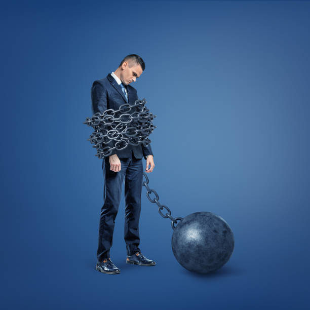 un triste uomo d'affari deluso è legato da un'ampia catena metallica che è bloccata a una palla di ferro. - debt trapped chain ball and chain foto e immagini stock