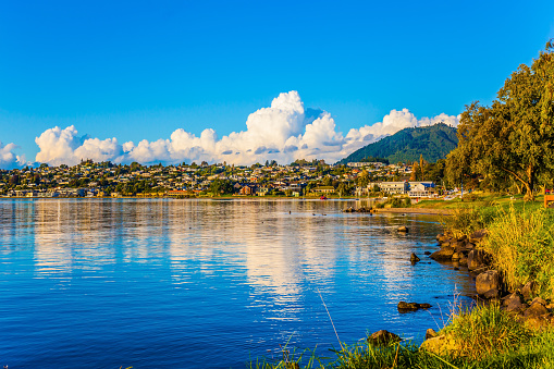 Fabulous summer sunset at Lake Taupo. Lush clouds and blue sky are reflected in the smooth water of the lake. The concept of active and phototourism