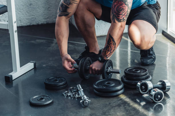 istock partial view of tattooed sportsman assembling dumbbells 1064972892
