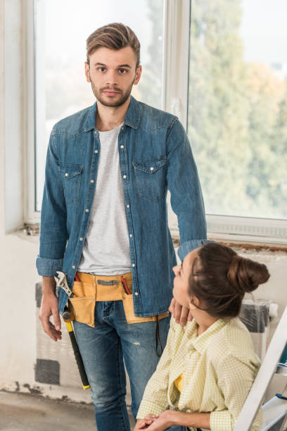 istock young man with toolbelt looking at camera while repairing apartment with girlfriend 1064981908