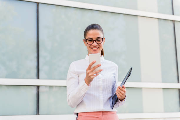 istock Successful young businesswoman using smartphone and holding documents outdoors. 1064982438