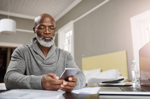 Smart apps make for smart budgeting Shot of a senior man using a mobile while working on his finances at home gray hair photos stock pictures, royalty-free photos & images