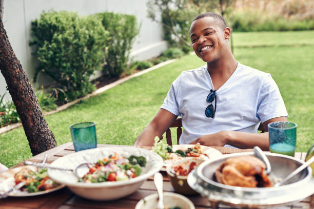 Nothing beats a leisurely Sunday lunch outdoors Shot of a young man having lunch in the backyard south african braai stock pictures, royalty-free photos & images
