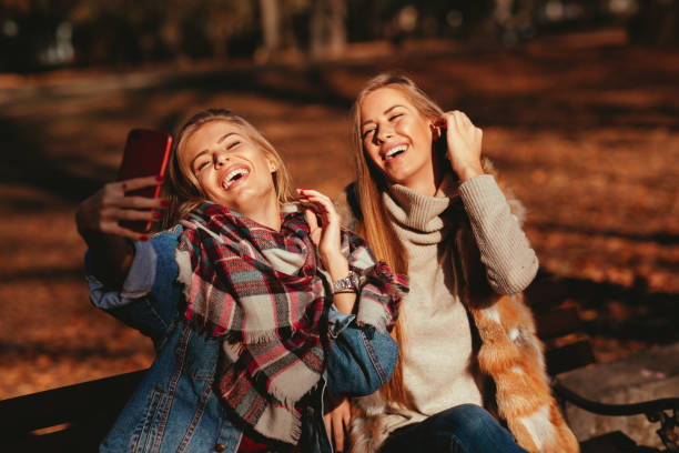 istock Two young women sitting on a bench and making selfie in the park 1065002462