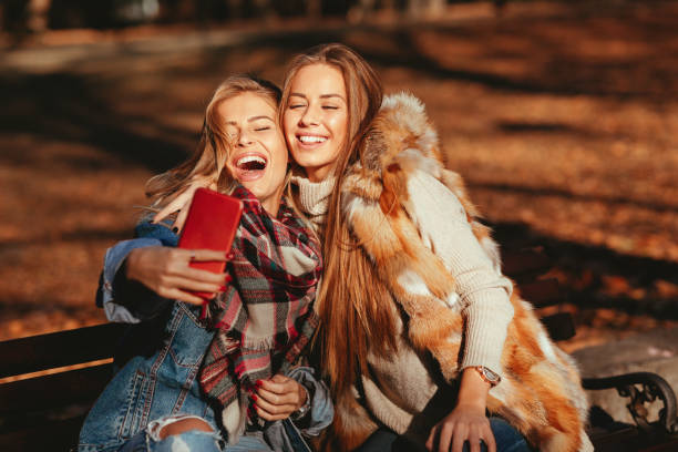 istock Two young women sitting on a bench and making selfie in the park 1065004624