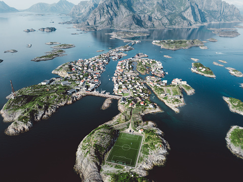 Drone photo of beautiful village of Henningsvaer, blue sea, mountains and stadium in Northern Norway