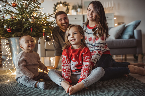 Young parents with kids celebrating Christmas at home and decorating Christmas tree. Home is decorated with Christmas ornaments and lights.