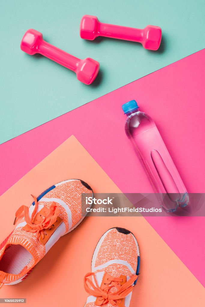 Endecha plana con zapatillas de deporte, pesas y botella sobre fondo colorido del deporte - Foto de stock de Ejercicio físico libre de derechos