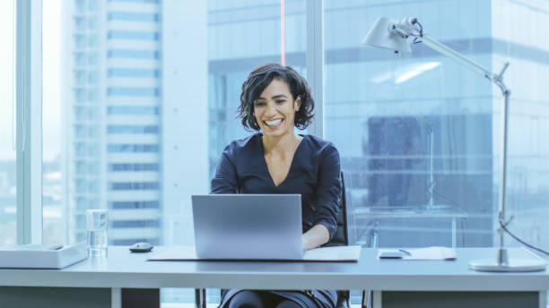 Beautiful Businesswoman Working at Her Desk in the Office with Cityscape Window View. Successful Woman Wearing Formal Wear Dress Working on a Laptop. Beautiful Businesswoman Working at Her Desk in the Office with Cityscape Window View. Successful Woman Wearing Formal Wear Dress Working on a Laptop. 'formal dress' stock pictures, royalty-free photos & images