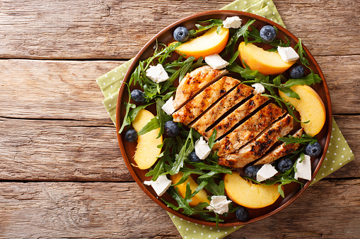 Grilled chicken breast with fresh peaches, blueberries, arugula and feta cheese close-up on a plate on a table. Horizontal top view from above