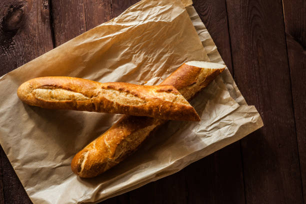 istock Fresh baguetteon paper bag, on wooden table, close up 1065099098