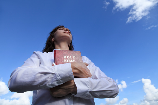 close up portrait of young woman holding Holy Bible over clear sky