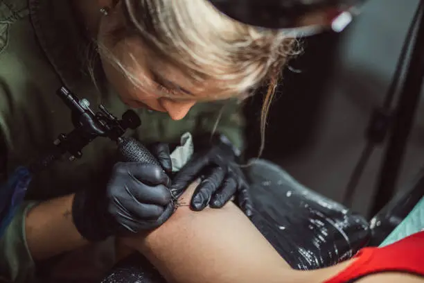 Two women in tattoo studio, woman is tattooing a woman's arm.