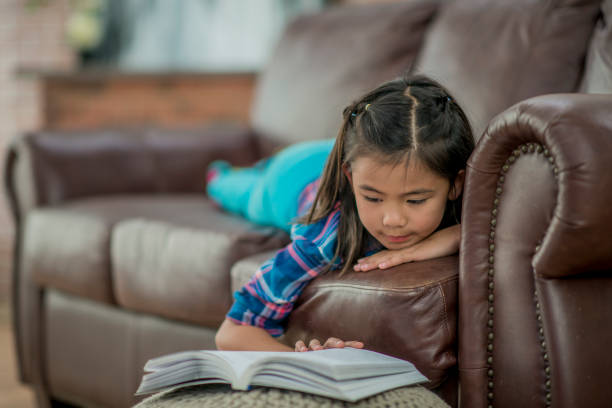 istock A little girl reads a chapter book on the sofa 1065141814
