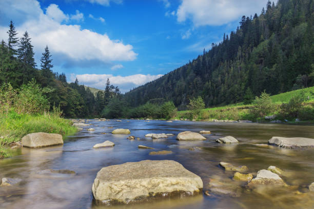 River in mountains with rocks, green grass on riverside. Mountain landscape, beautiful sky, clouds. Idea for outdoor activities, travel .