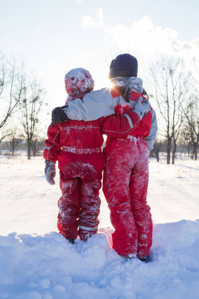 Two smiling boys in winter clothes standing together at the snow on the winter park