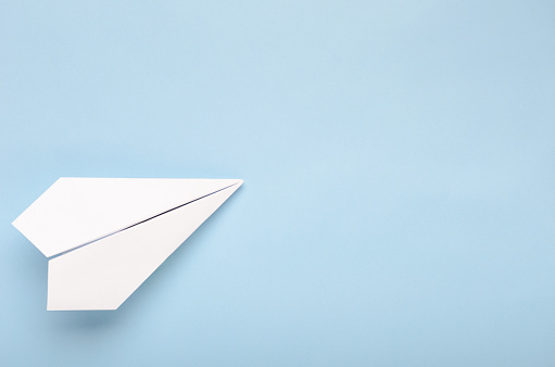 Paper plane on a blue background. Concept of flight, travel, transfer. Top view, copy space, flat lay.