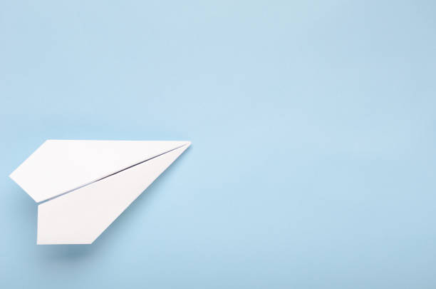 Paper plane on a blue background. Concept of flight, travel, transfer. Top view, copy space, flat lay Paper plane on a blue background. Concept of flight, travel, transfer. Top view, copy space, flat lay. paper airplane photos stock pictures, royalty-free photos & images