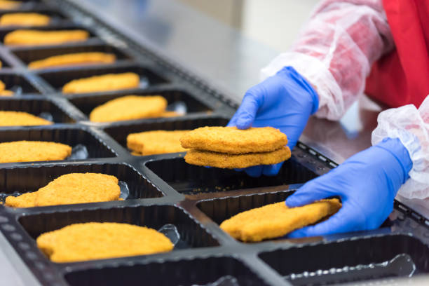 The worker in the factory places the chicken schnitzel stock photo