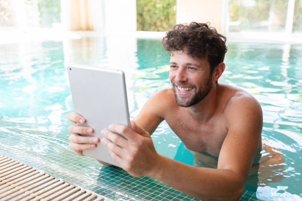 istock Young man on his vacation enjoying the pool while looking at something on tablet very happy 1065161010