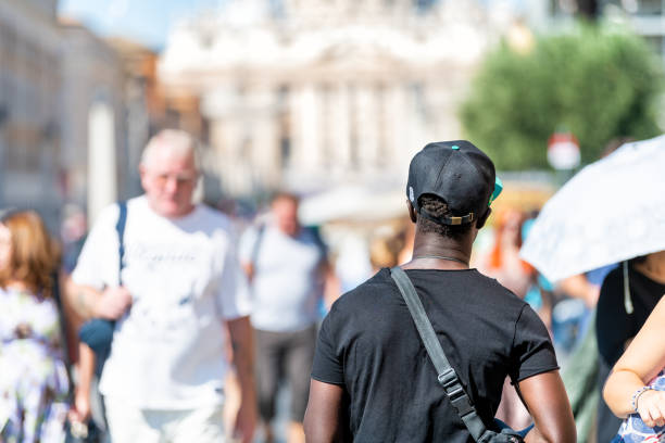 maschio nero africano, uomo, immigrato che cammina per strada, strada con molti italiani, città del vaticano, basilica di san pietro, piazza - st peters square foto e immagini stock