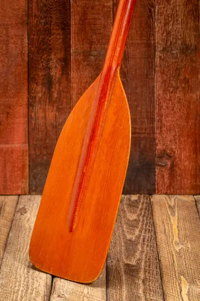 wooden blade of a canoe paddle against rustic barn wood