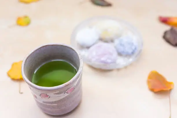 Green tea cup and mochi rice cake Japanese dessert wagashi, colorful daifuku, autumn season leaves on table, vibrant color