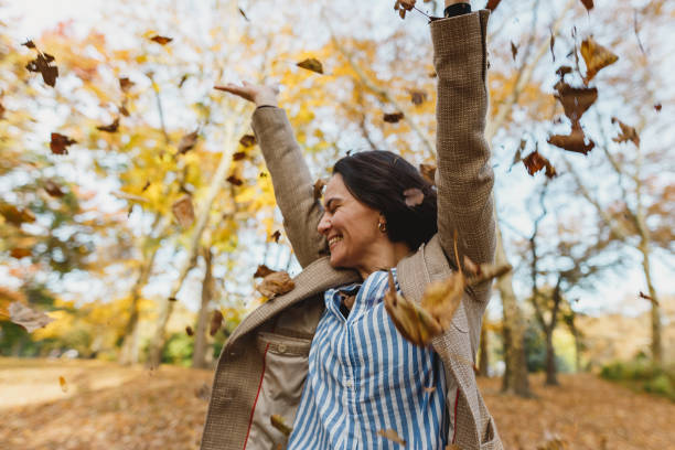 mujer tirando otoño deja en el parque central - autumn leaf falling wind fotografías e imágenes de stock