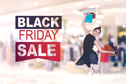 Female dancer holding shopping bags while jumping with Black Friday Sale text