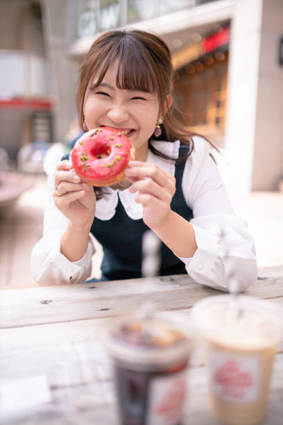 glückliche junge frau mit donut im offenen café - harajuku district stock-fotos und bilder