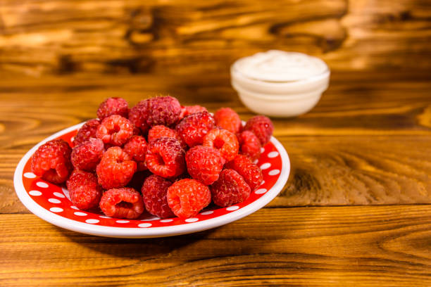 istock Ceramic plate with ripe raspberries and sour cream on wooden table 1065196902