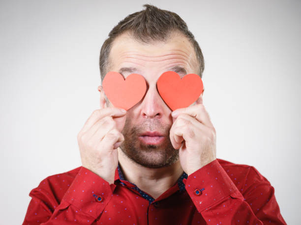 Adult serious man covering eyes with red hearts. Male blinded by love. Romance feelings valentines day concept